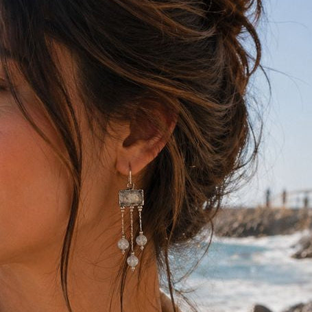 Woman with beach hair and earrings standing by the ocean